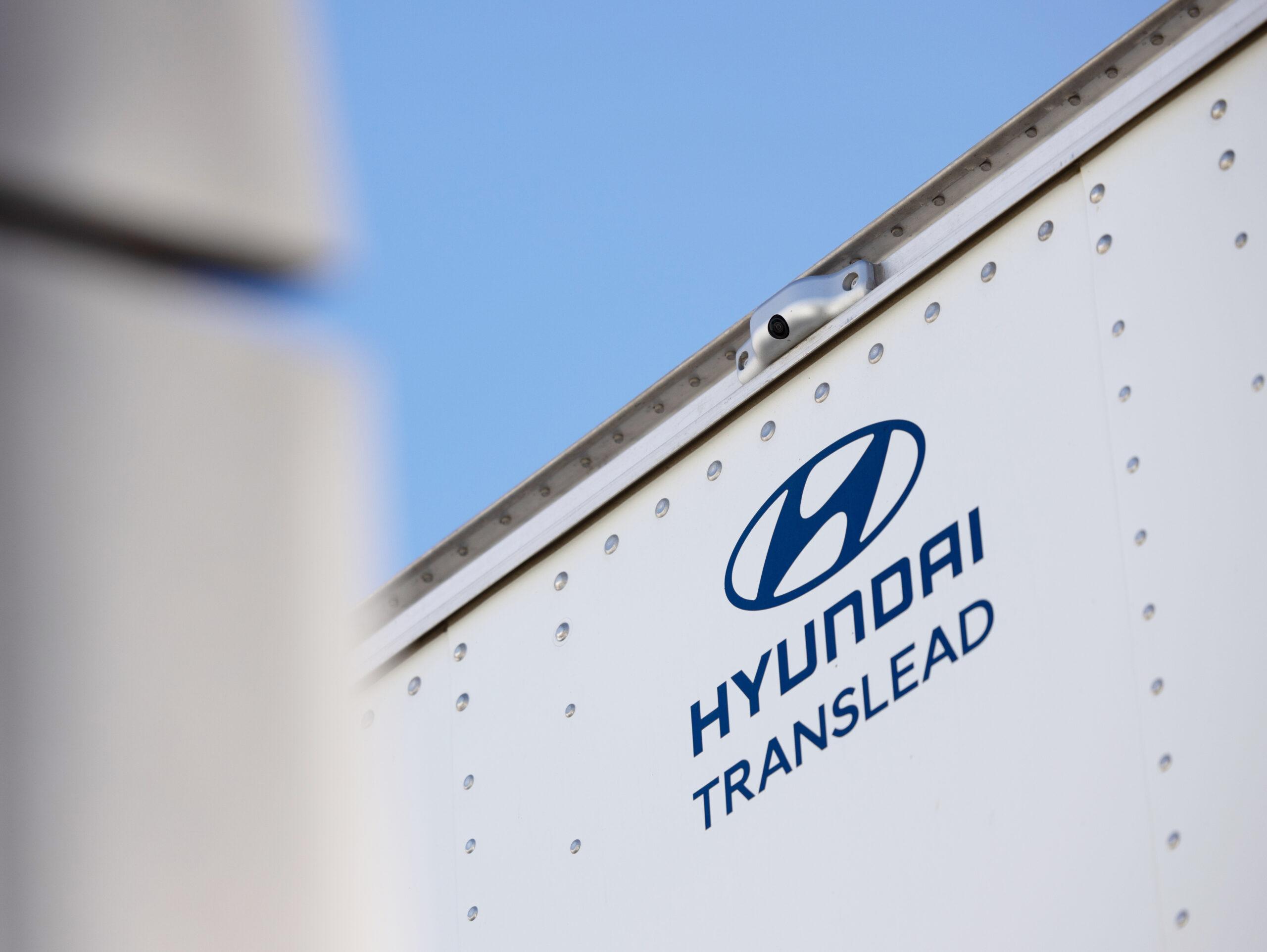 DIN6821_02169_v2 (1) Close-up of the Hyundai Translead logo on a white trailer side, featuring an HT LinkVue camera system, highlighting Hyundai's innovation in trailer technology for improved visibility and incident recording.