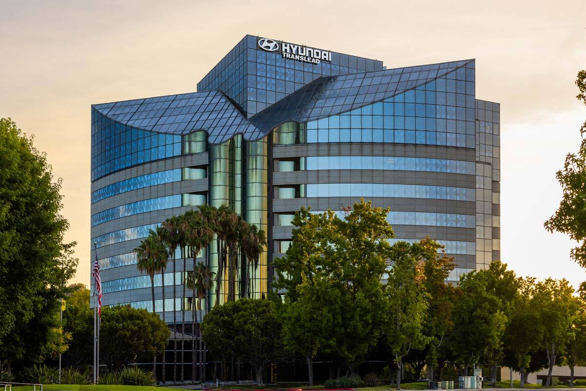 mobile-contact The modern glass building of Hyundai Translead, with its logo prominently displayed, surrounded by trees and palm trees under a clear sky, representing Hyundai's corporate presence and its commitment to transportation technology.